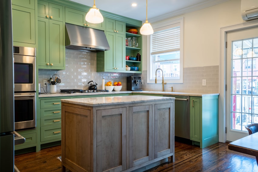 A kitchen with deep green cabinetry and a marble-topped island